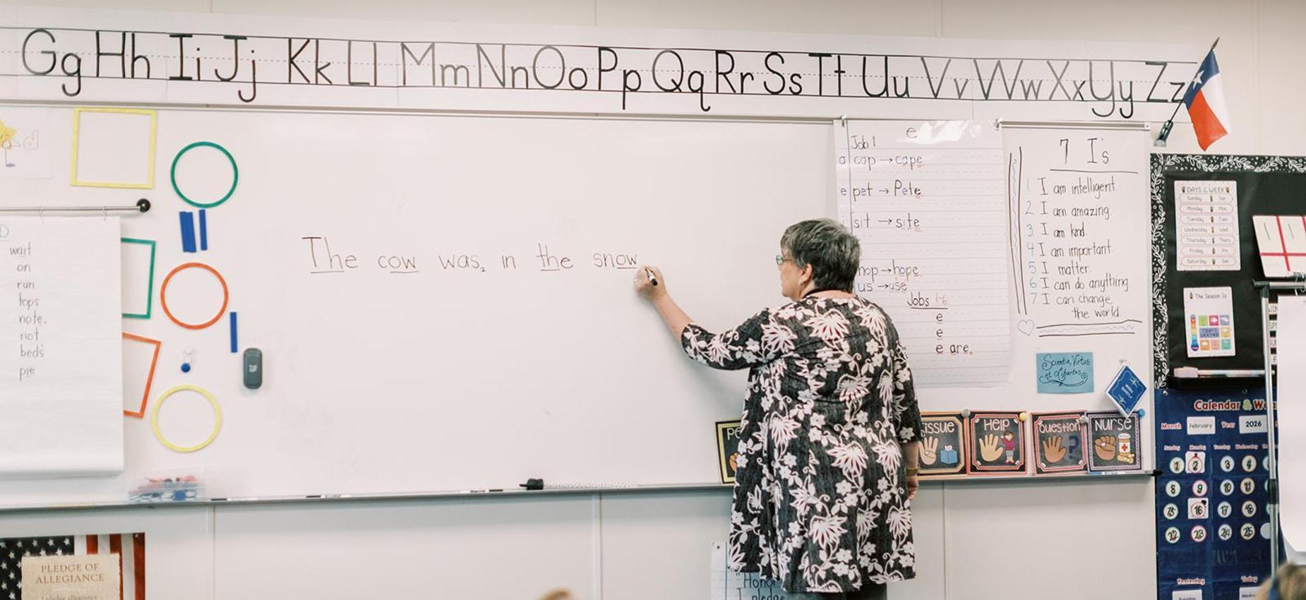 Teacher writes a sentence on the whiteboard for an elementary class