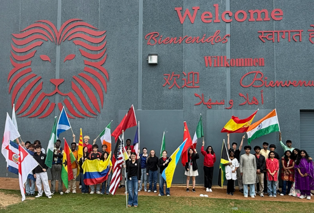 Students stand in front of the Welcome wall (with welcome in 7 languages) holding flags