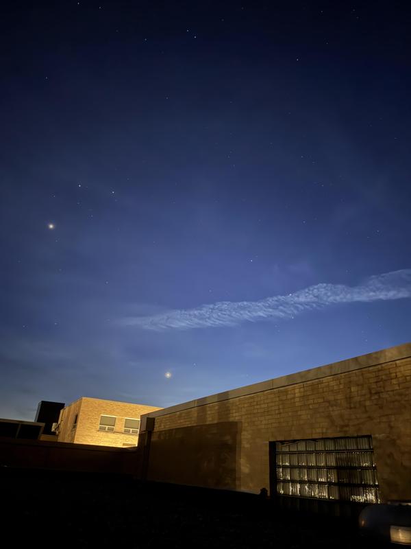 Night sky with stars and a wispy cloud over a building.