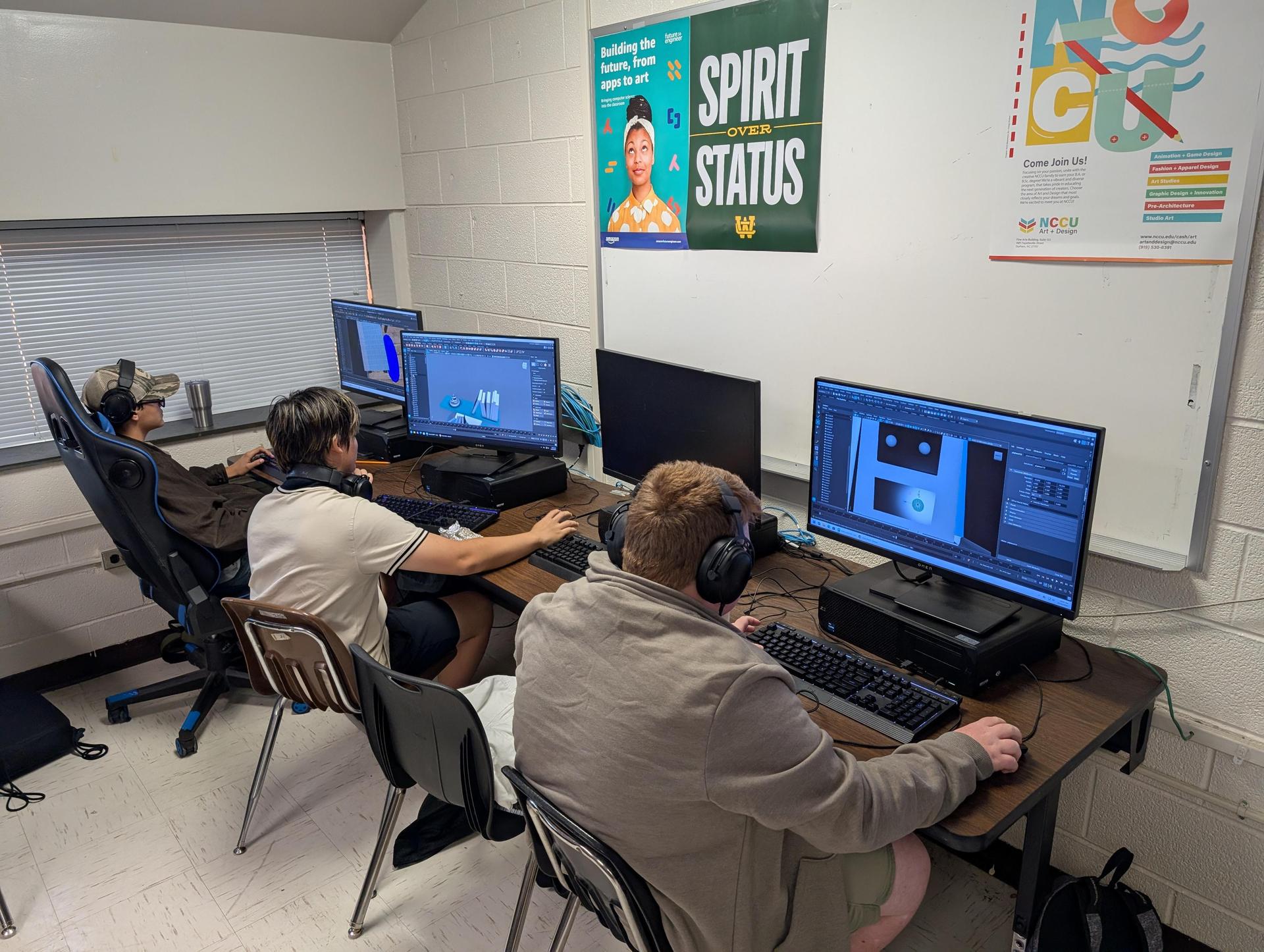 Three students working on computers in a classroom, wearing headphones.