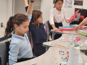 A fourth grade girl raises her hands to show she has the correct answer.