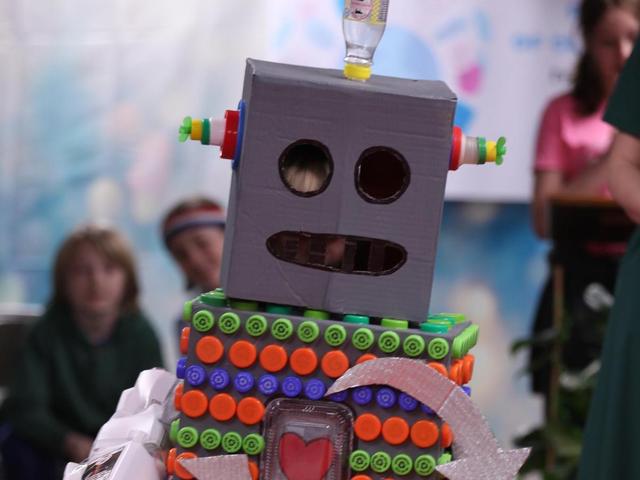 A handmade robot made from cardboard and colorful materials stands in a vibrant environment.