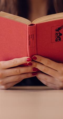 A person holding a red book with painted nails.