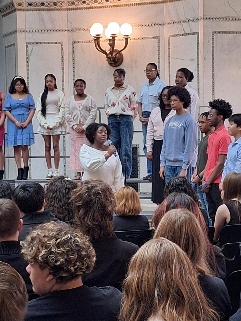 Choir singing in front of seated crowd.