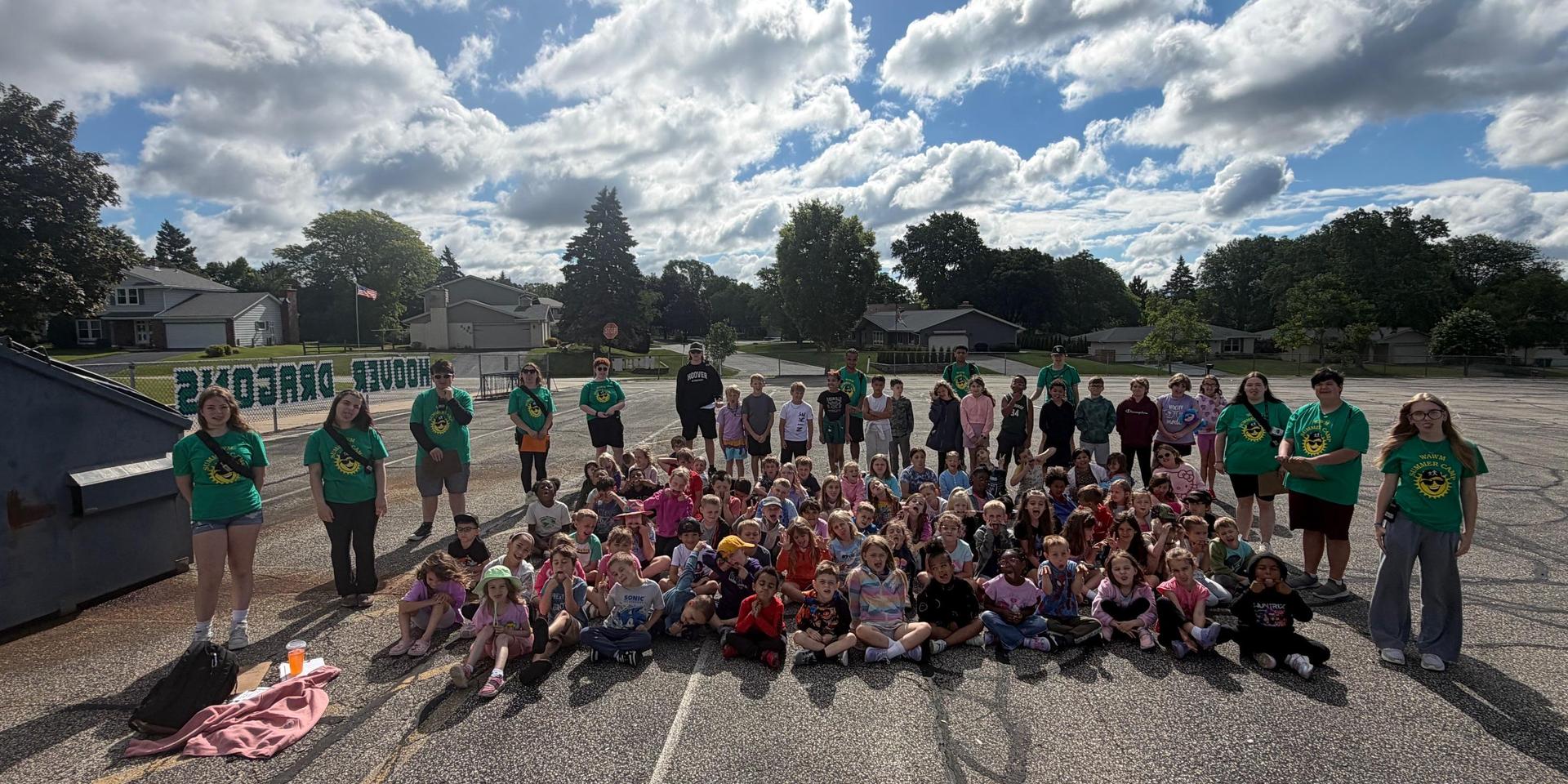 A large group of children and adults gathered outdoors on a sunny day.