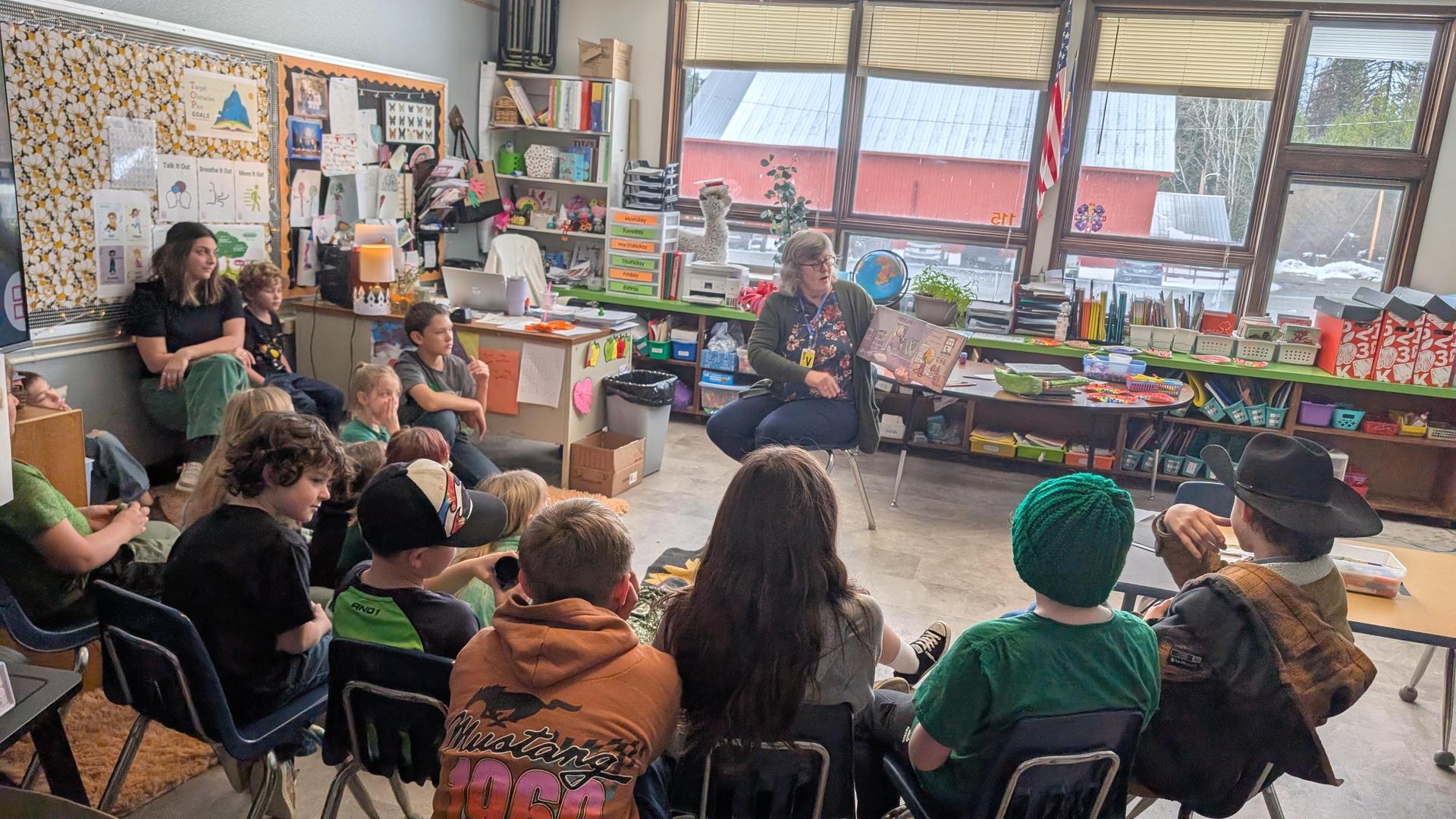 Classroom scene with a teacher reading to students sitting on chairs, engaged and attentive.
