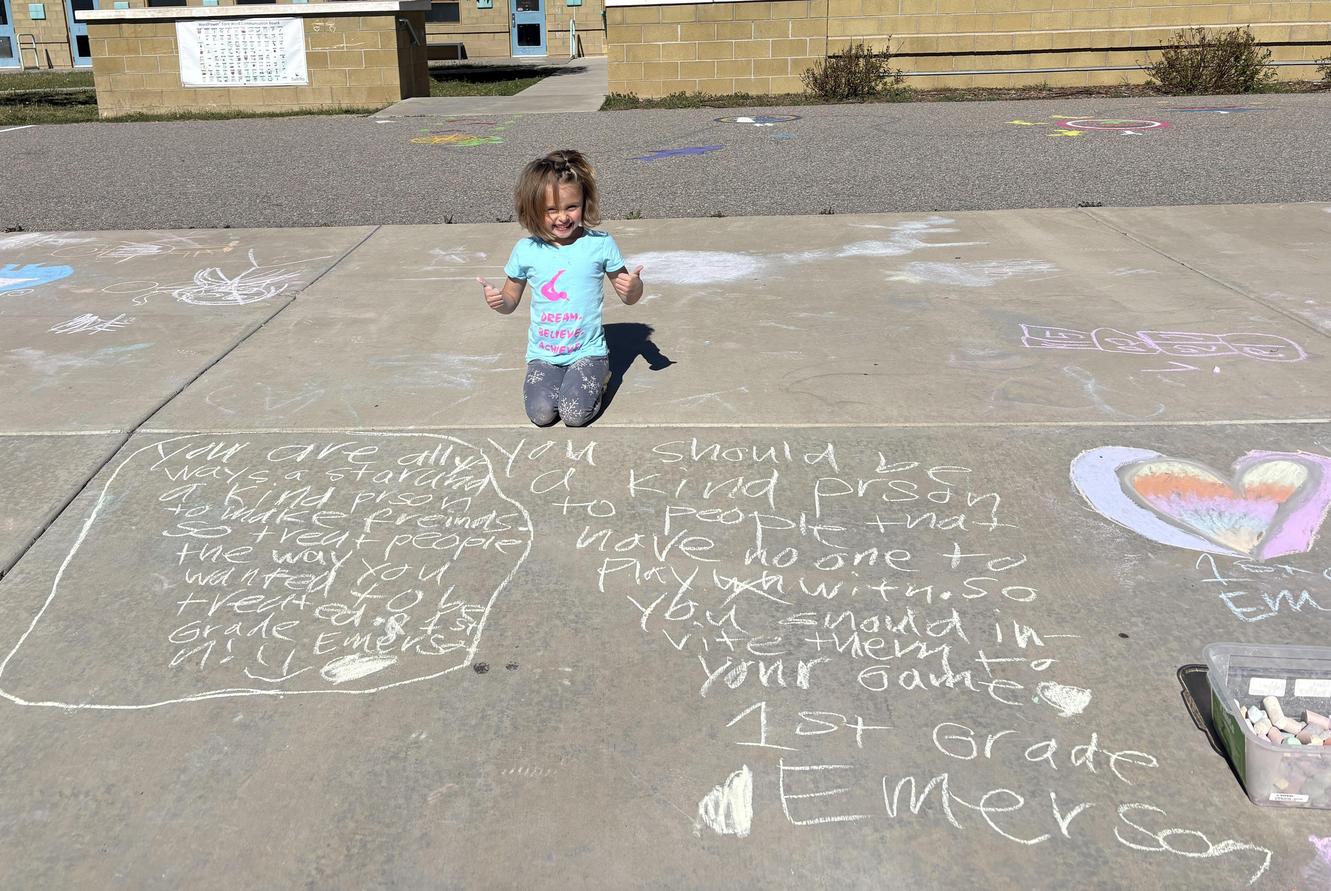 Child kneeling on pavement with chalk drawings and notes for classmates.
