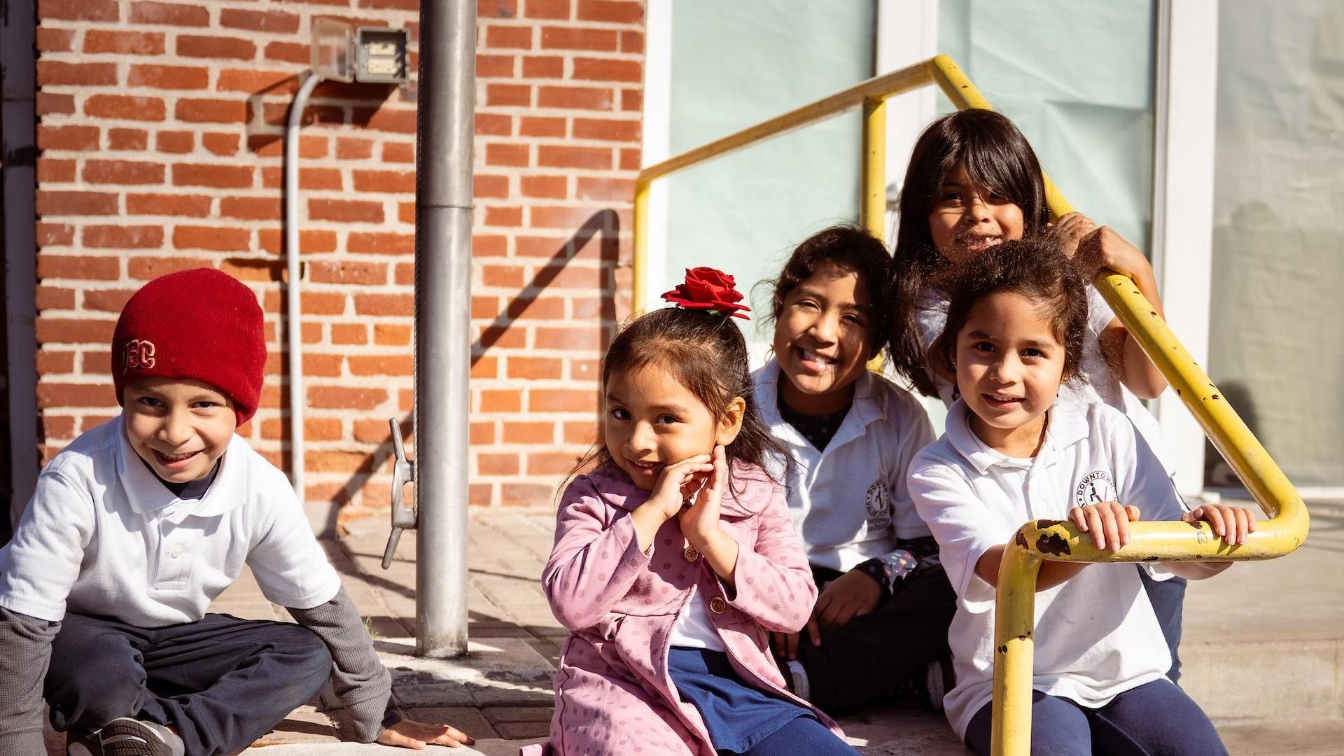 A group of children sitting on stairs, smiling, with a red flower in one girl's hair.