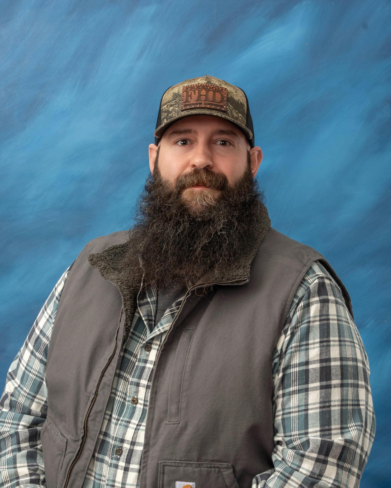 Photo of Mr. Trevor McIntyre wearing a gray vest in front of a blue background.