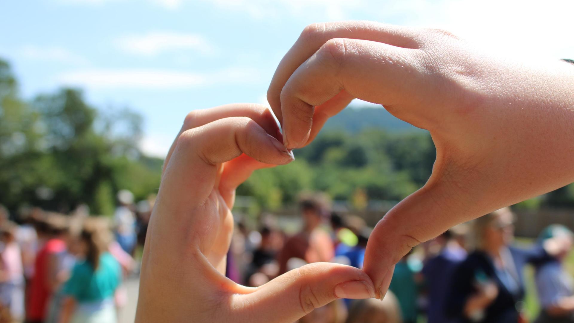 Hands making a heart shape, with children, blurred in the background