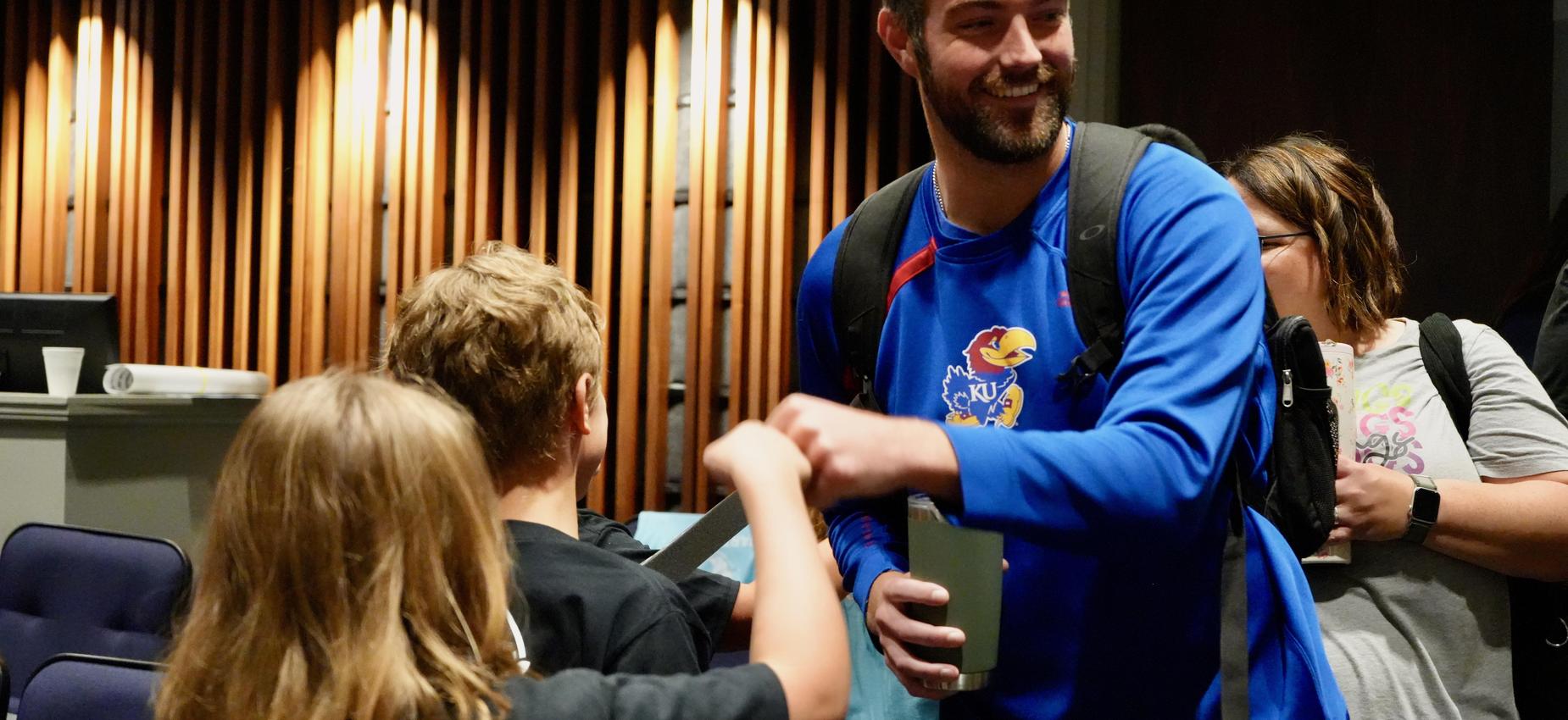 Man shaking hands with children in a warmly lit venue.