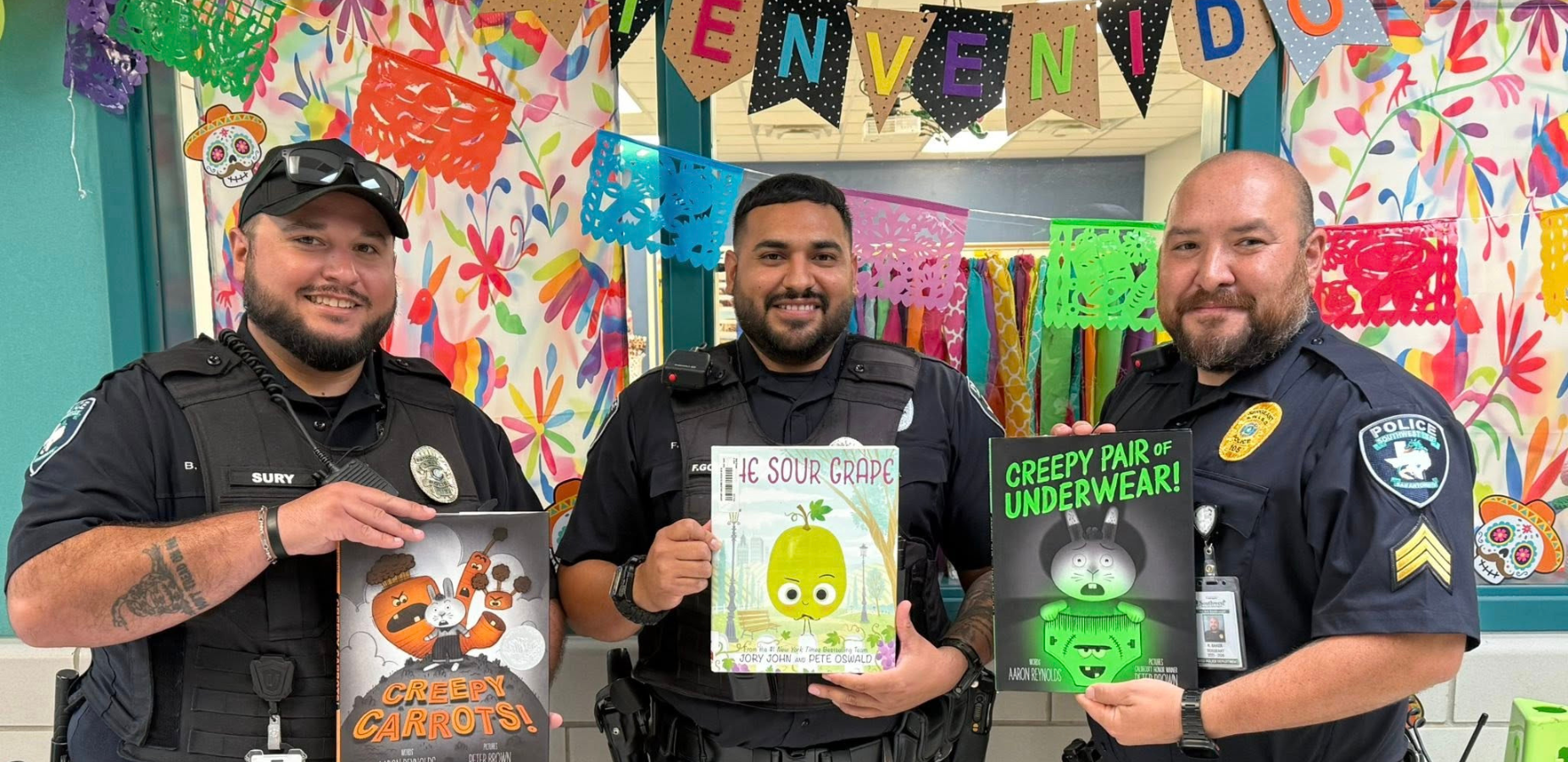 3 male police officers wearing blue uniforms and holding children's books