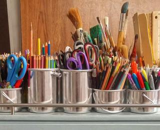 Cups filled with colorful pencils and brushes in an art workspace.