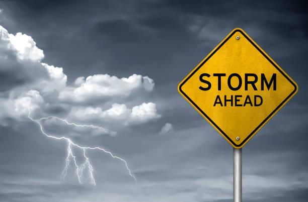 Yellow warning sign stating 'STORM AHEAD' beside dark stormy clouds and lightning.