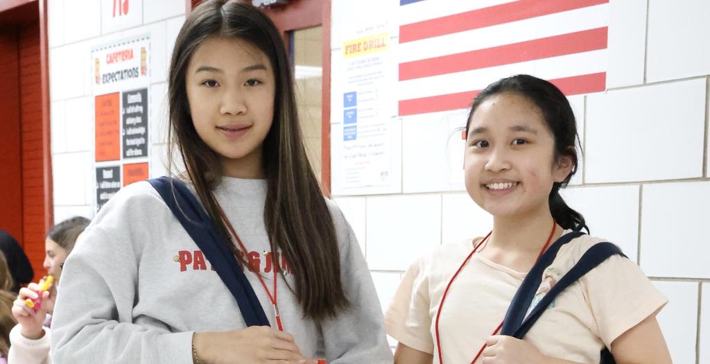 Two girls standing near a wall that has the American flag