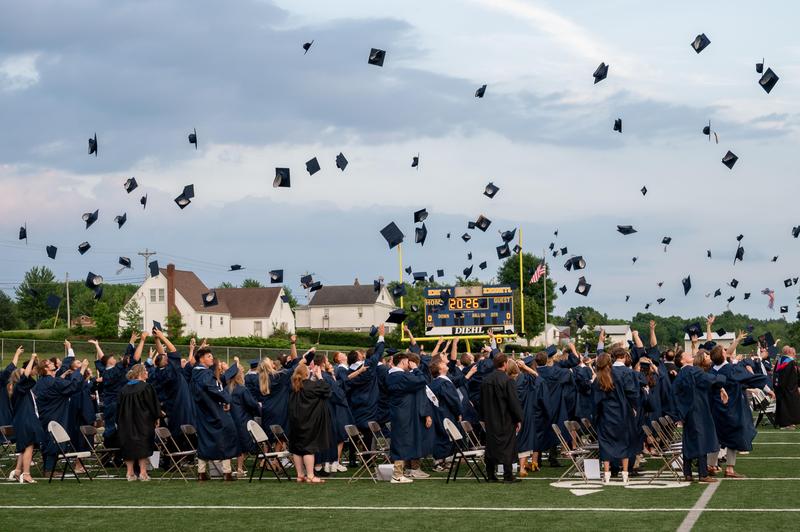 graduate caps fly in the area with 2026 on the scoreboard behind them