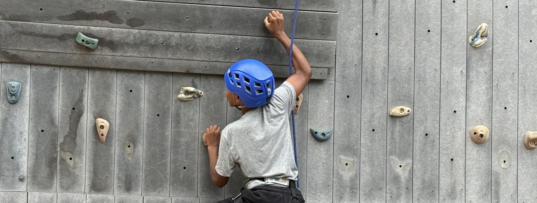 A person climbing a rock wall, wearing a blue helmet and harness.