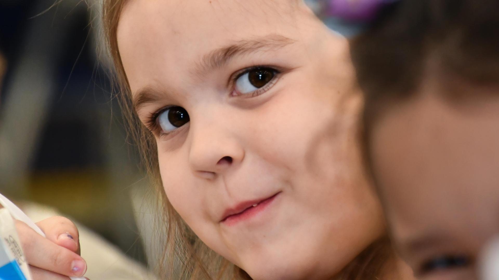 A close-up of a girl smiling softly while enjoying a snack with friends.