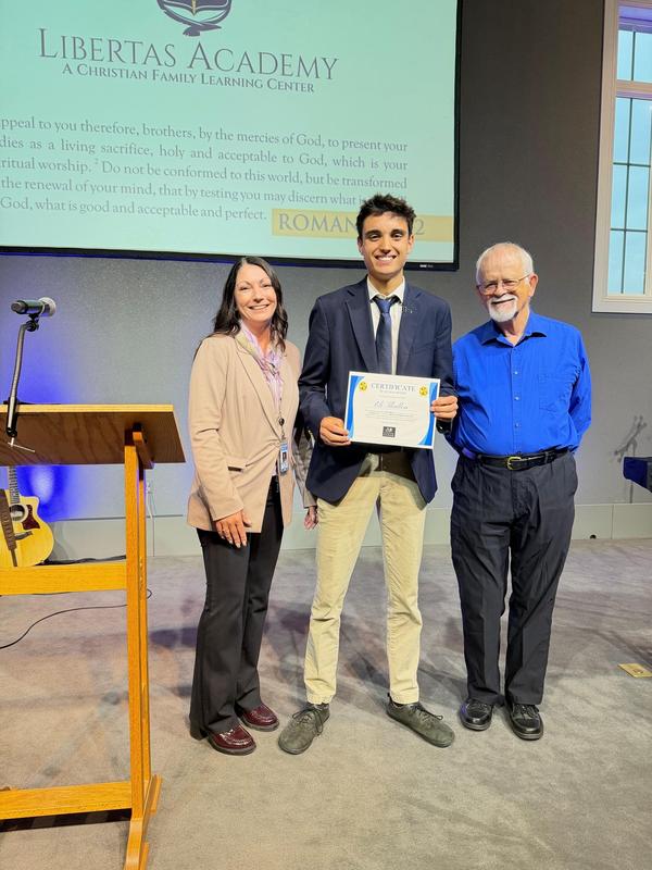 woman and older man presenting scholarship to male high school senior