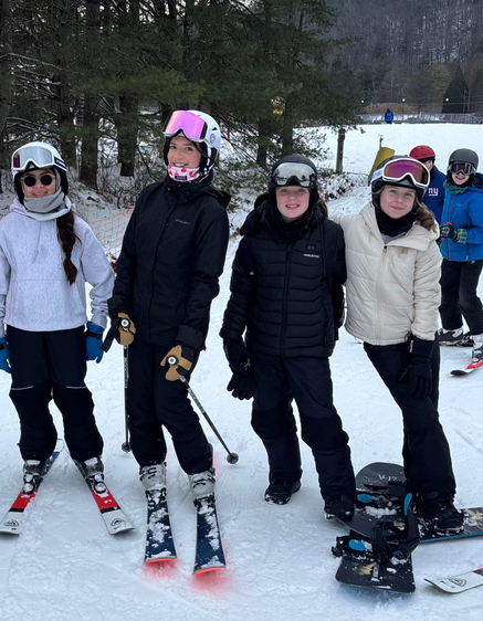 Four skiers standing on a snowy slope, wearing winter gear and ski equipment.