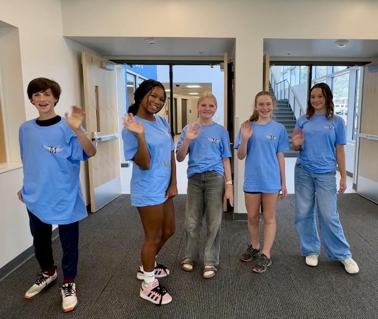 Five students post in blue t-shirts and wave to the camera