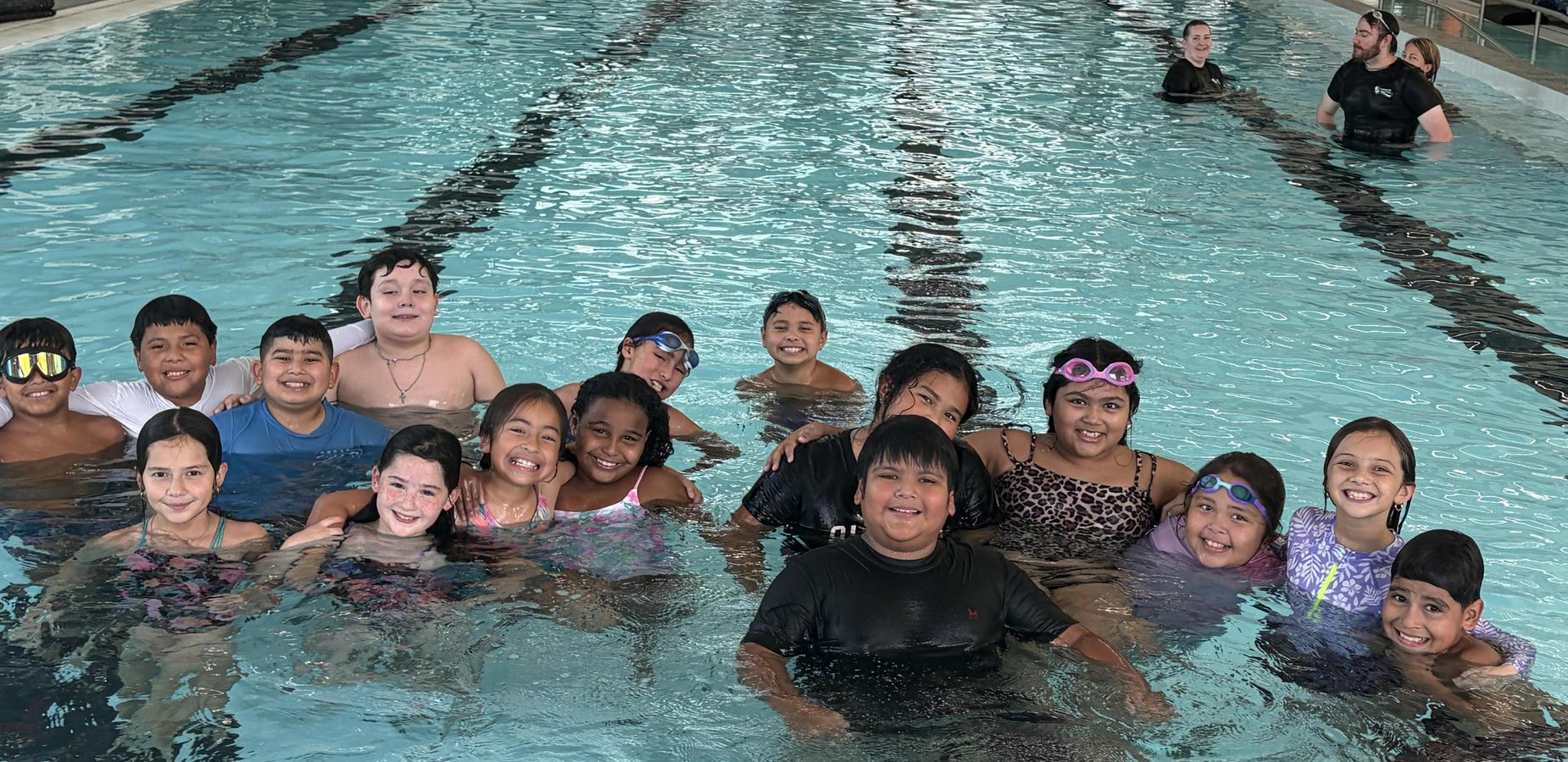 A group of children smiling while swimming in a pool during a swimming session.