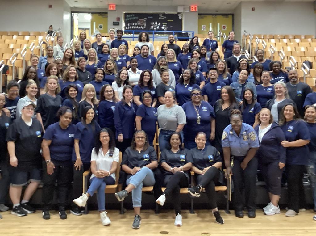 Large group of diverse staff members gathered in an auditorium, smiling at the camera.