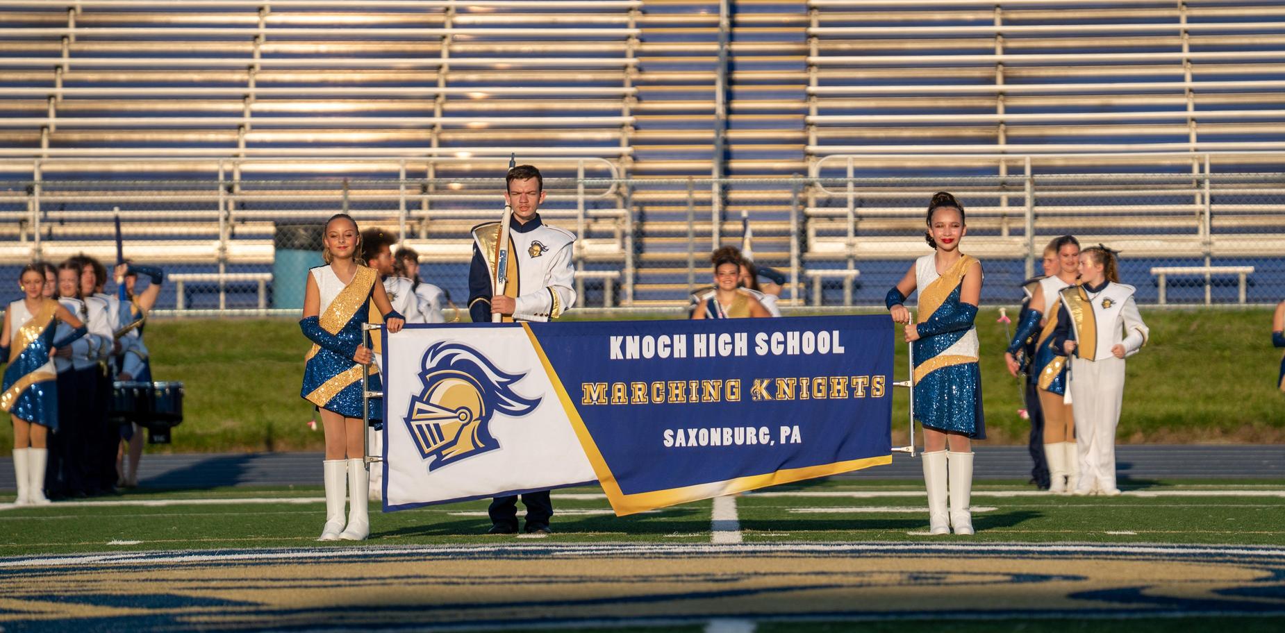 A group holding a banner for Knoch High School, showcasing performers in uniform.
