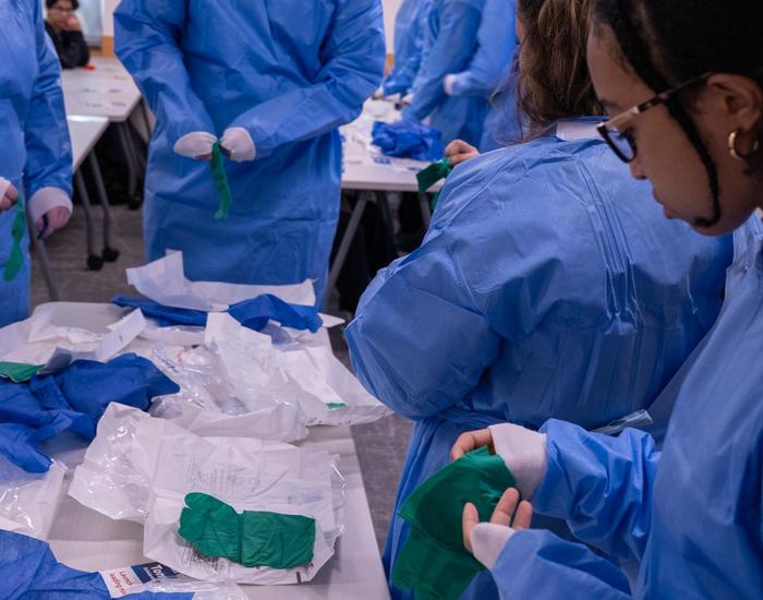 Students learning how to put on scrubs and gloves