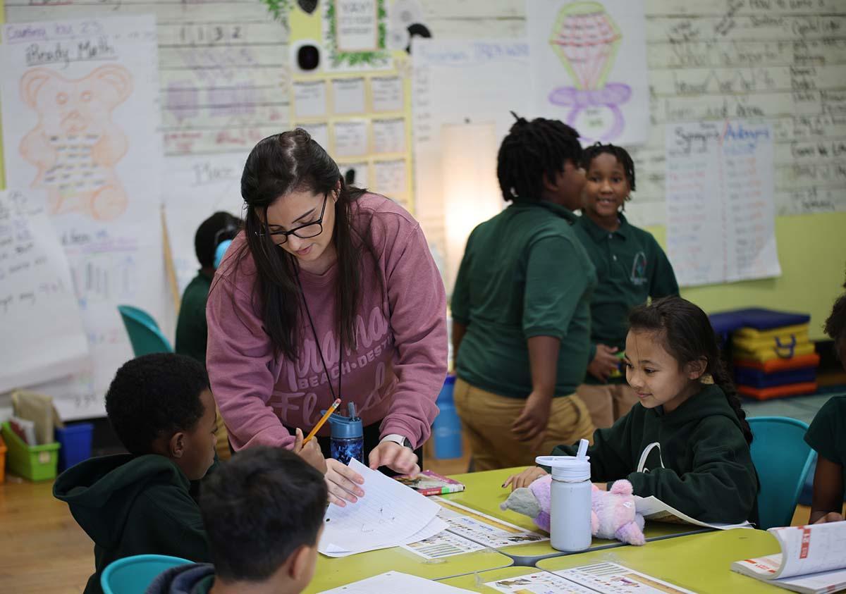 HSA Teacher smiles while kneeling beside a young student in a classroom setting.