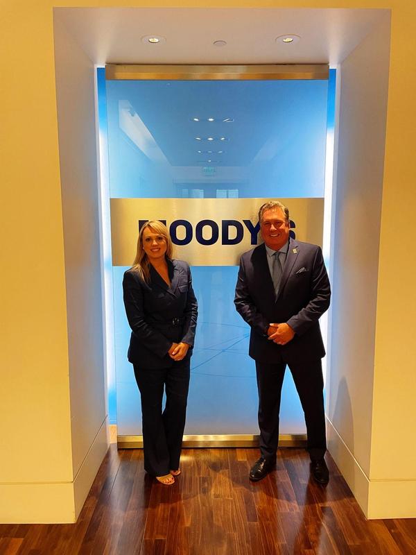 Superintendent Brinda Leon (left) and Assistant Superintendent Rick Champion (right) stand in front of a colorful light blue and yellow wall. The word Moodys is painted on the back of the wall.