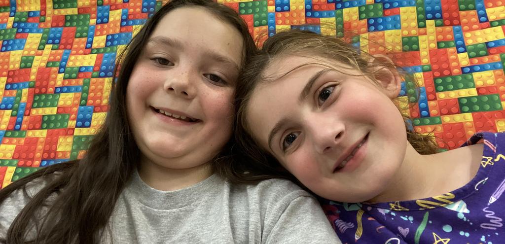 Two girls smile together in front of a colorful background.