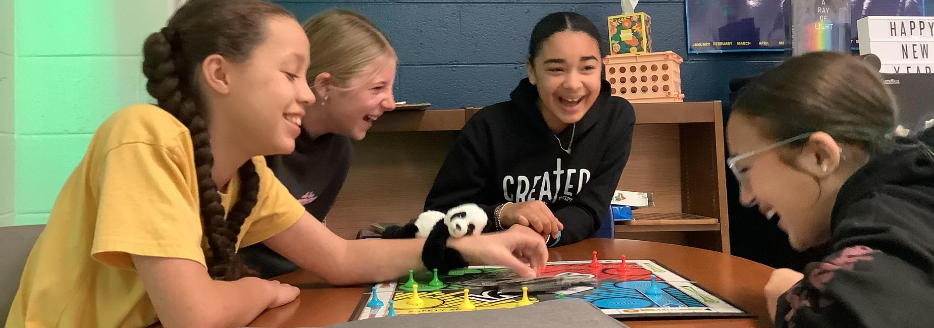 Four girls laughing and playing a board game together at a table.