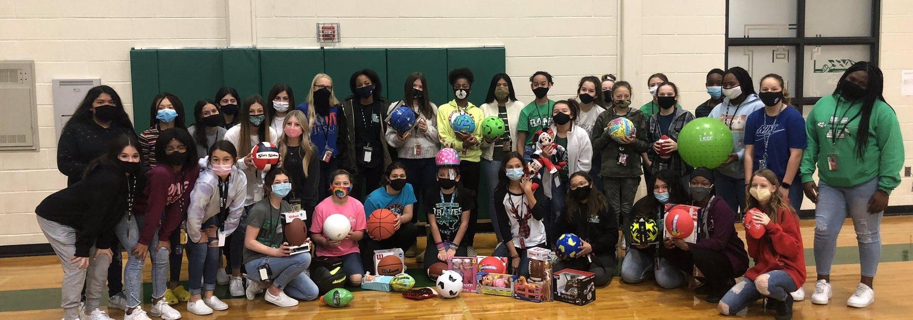 large group of female athletes holding balls to be donated to those in need