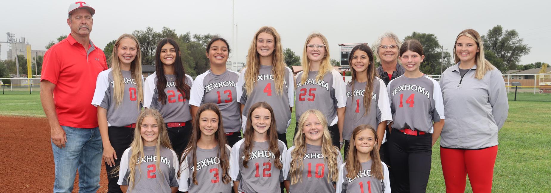 Group of girls in gray and red softball uniforms posing with a coach.