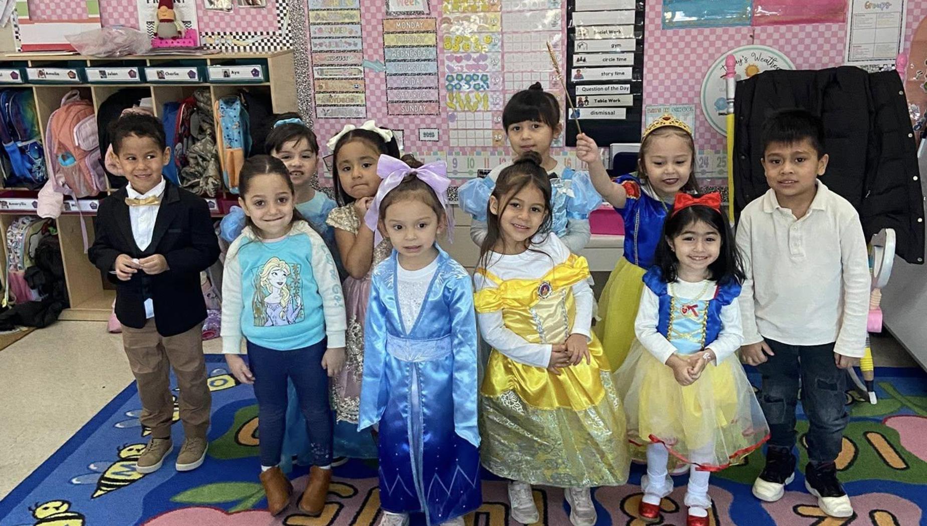 Group of children dressed in princess costumes posing together in a colorful classroom.