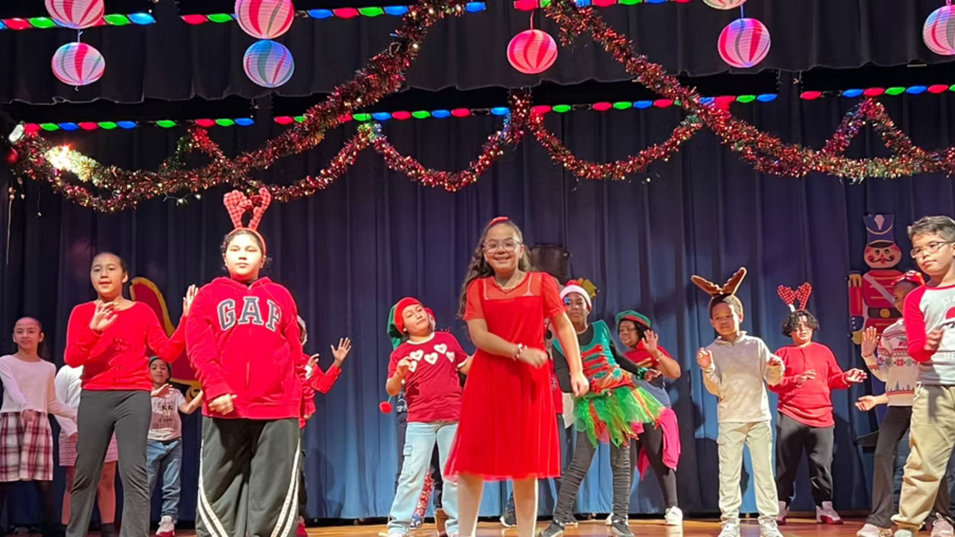 Children performing on stage in festive attire with decorations.