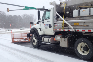 A snow plow sits at a snowy intersection with its blade down.