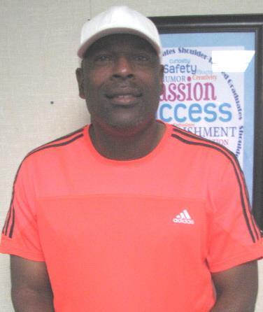 Man wearing an orange Adidas shirt and white cap, smiling against a decorative wall.