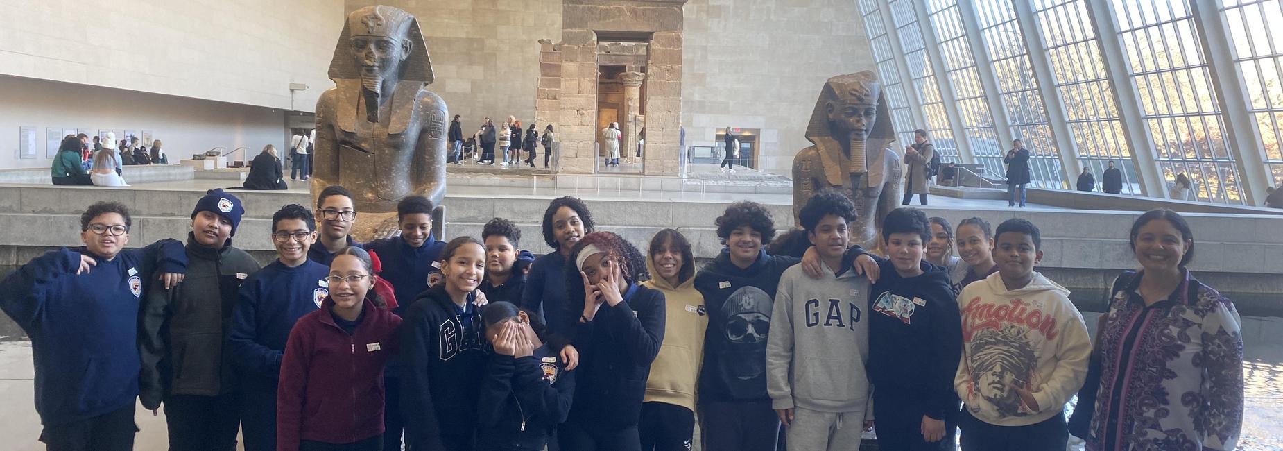 Group of children posing with ancient statues in a modern museum interior.