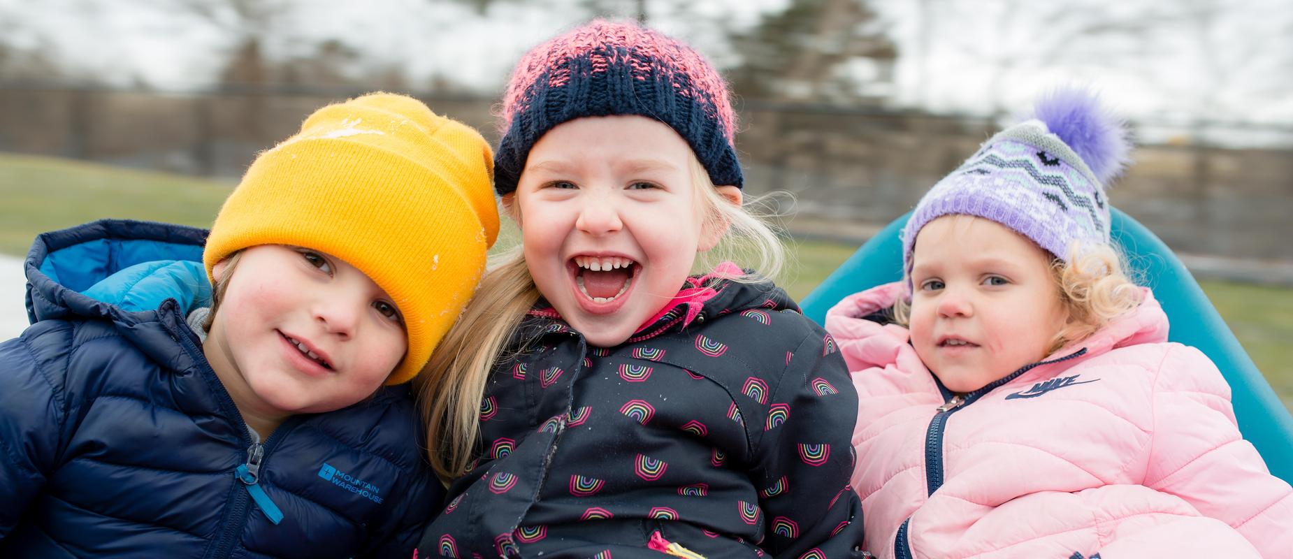 3 preschoolers on playground in their winter hats and jackets