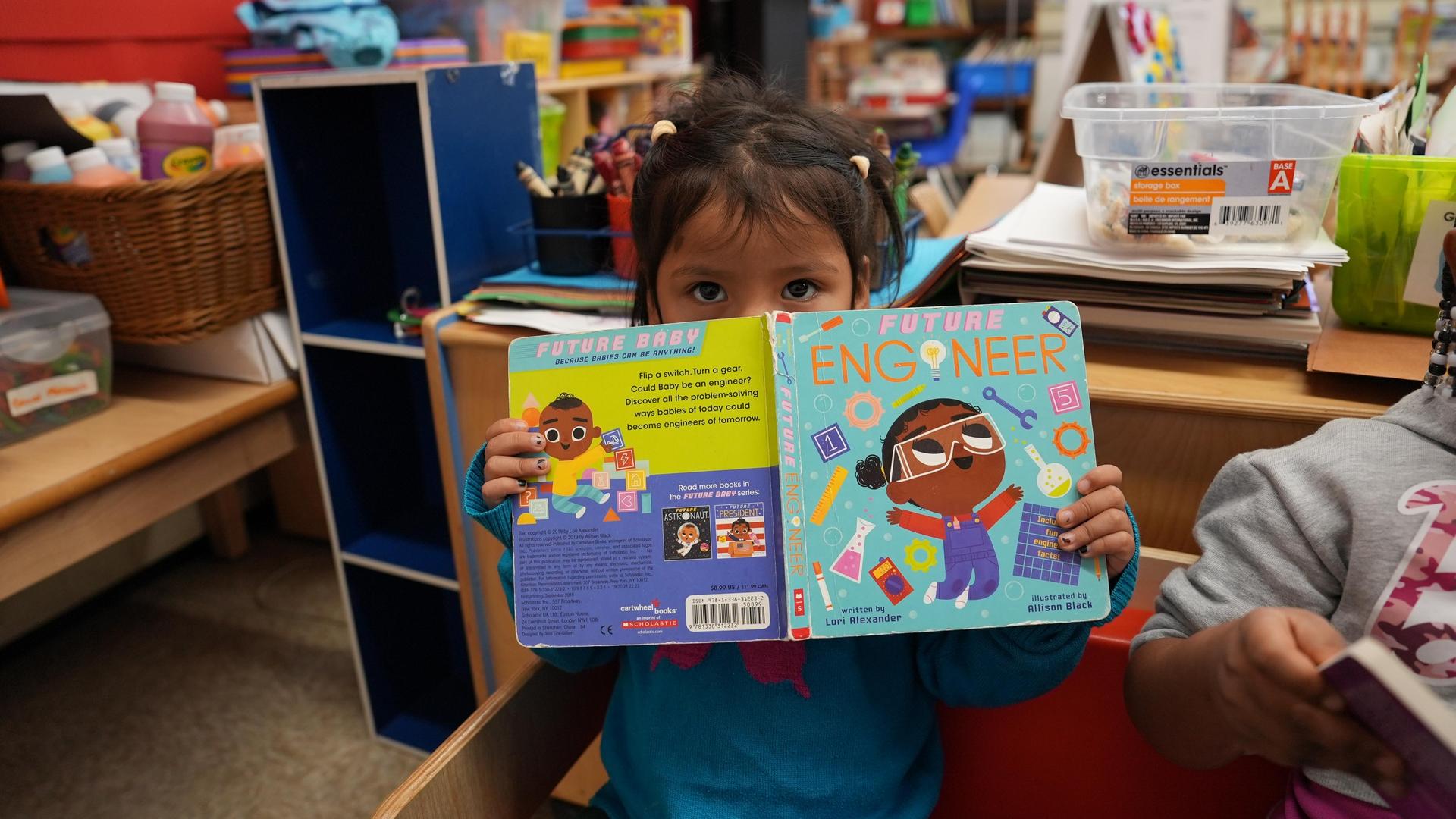 Child holding a book titled 'Future Engineer'.
