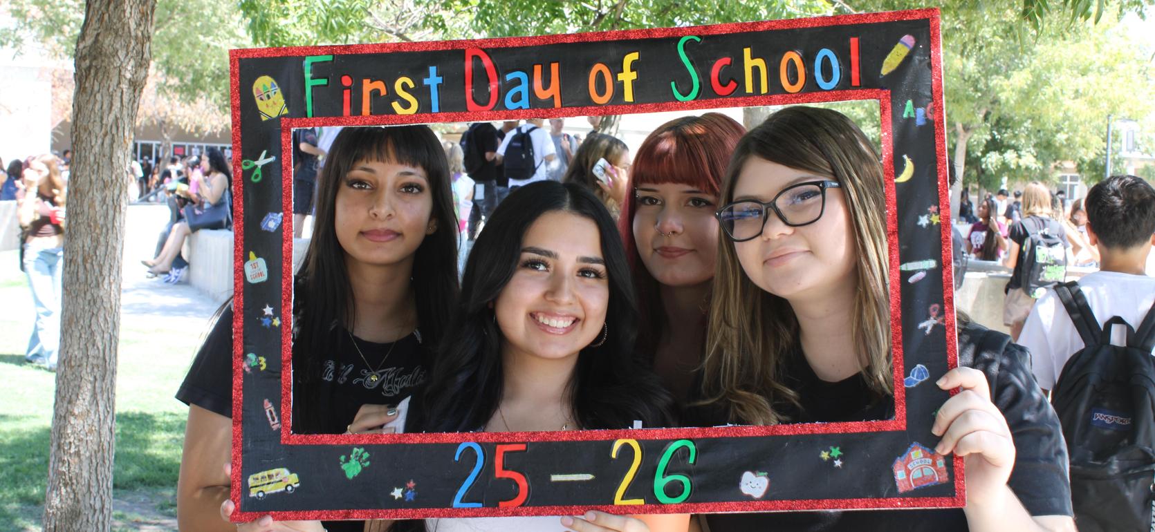 Four girls holding a frame that says 'First Day of School' with decorations.