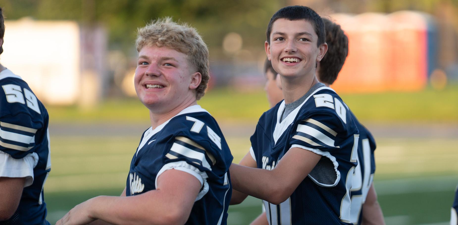Two football players smiling at the camera, standing close together.