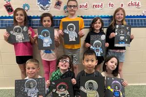 Students hold up a self-portrait they created with astronaut theme