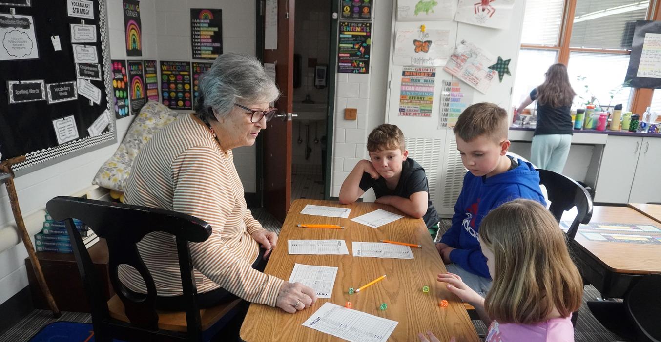 A group of four children seated at a table, engaged in an activity with an adult.