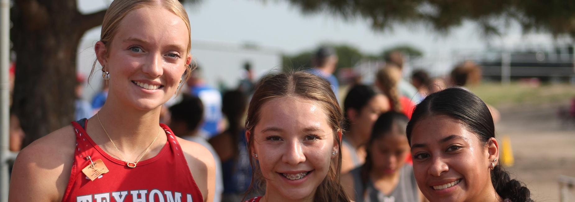 Three female athletes posing together, smiling, wearing matching red uniforms.