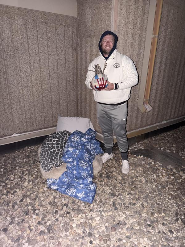 Man holding a decorative glove stands beside cushions on the ground.