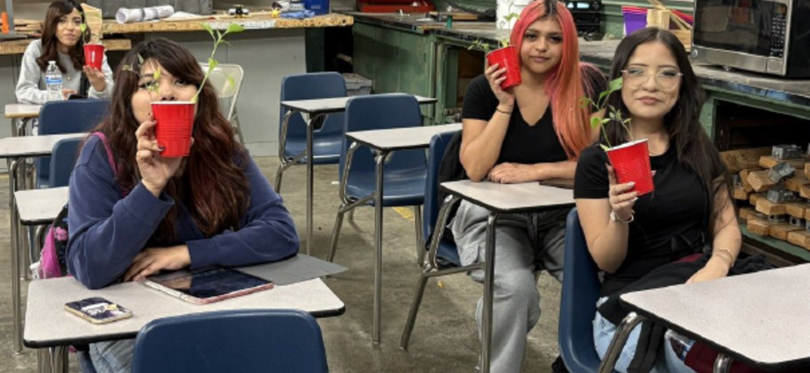 Four students sitting in a classroom holding cups with small plants.