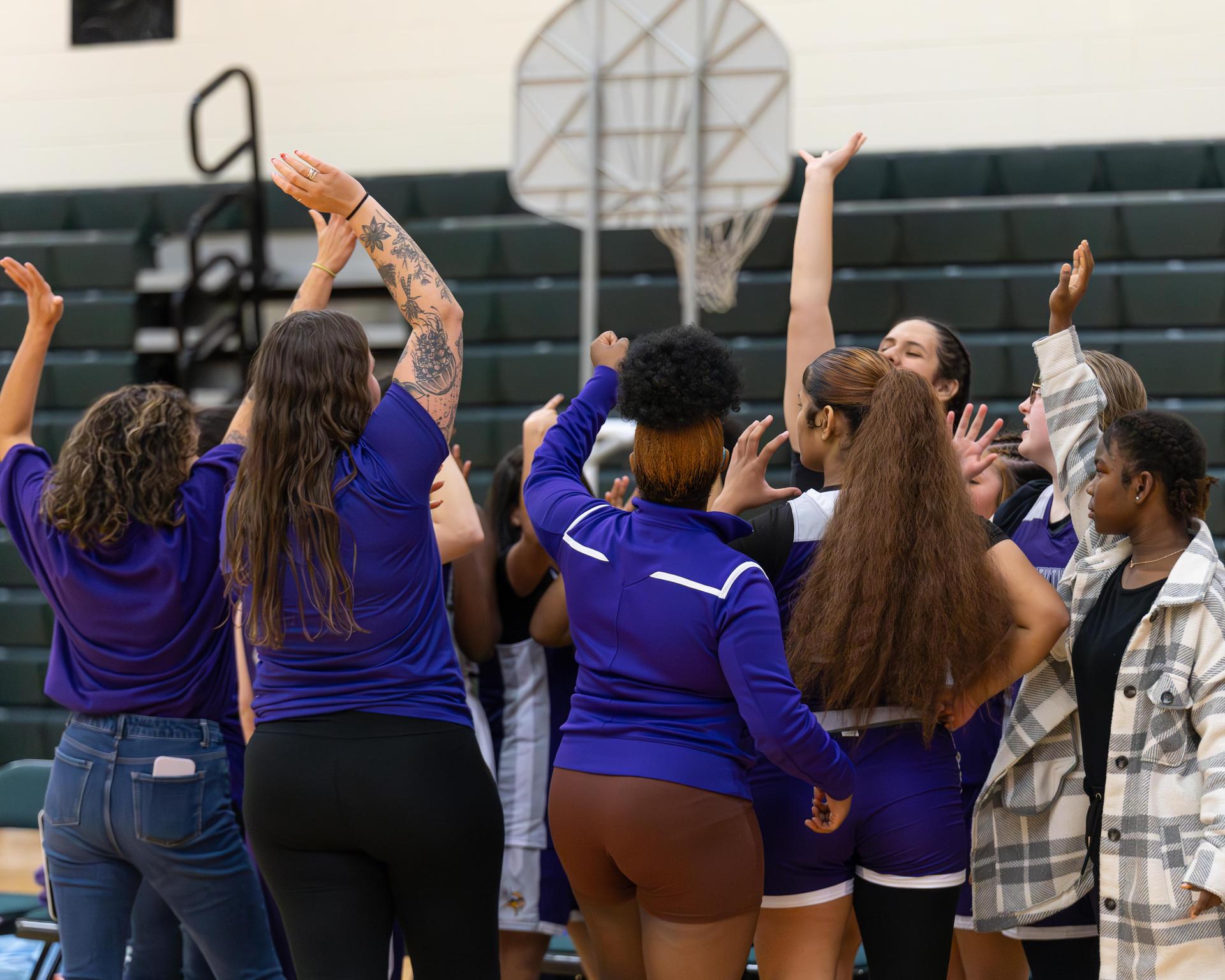 The varsity girls basketball team cheering in a huddle.